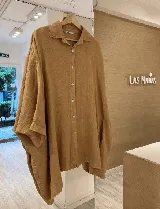 Camisa de lino de corte oversize y silueta amplia, con cuello clásico, cierre frontal de botones de nácar y bolsillos laterales invisibles.