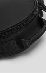 Bolso circular de estructura rígida, color negro, diseñado para el transporte de auriculares y accesorios. Cuenta con manija superior reforzada, correa de hombro ajustable con logo grabado, cierre perimetral y bolsillo trasero de acceso rápido.
