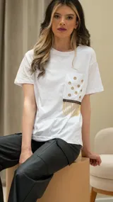 Remera blanca de algodón con cuello redondo y mangas cortas. Presenta un bolsillo en el pecho con apliques de strass dorados y flecos.