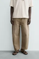Jeans de hombre, tiro medio, color marrón claro o caqui, con corte relaxed fit y perneras anchas. Presenta cinco bolsillos y costuras laterales giradas hacia el frente.