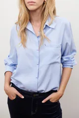 Camisa blanca de manga larga con cuello clásico, cierre de botones frontal y bolsillo de parche en el pecho.