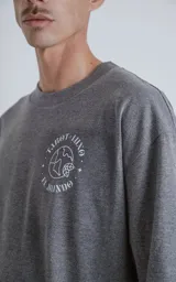 Remera de corte oversize color gris melange, con cuello redondo y mangas cortas. Presenta un estampado en la espalda inspirado en la carta del tarot 'El Mundo', con diseño gráfico detallado y tipografía alusiva.