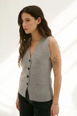 Chaleco tejido de punto en color beige, con escote en V, cierre frontal con botones oscuros y bolsillos frontales decorativos.