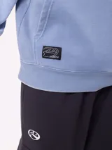 Canguro con capucha de calce holgado, color azul con efecto lavado. Presenta bolsillo frontal tipo canguro, logo de la marca estampado en el pecho y etiqueta pequeña en el ruedo.