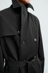 Trench de corte regular confeccionado en tejido técnico italiano repelente al agua. Presenta cuello con solapas de muesca, cierre frontal de botonadura cruzada, cinturón ajustable del mismo tejido, bolsillos de vivo en la cadera, manga larga con puños ajustables y abertura central en la espalda.