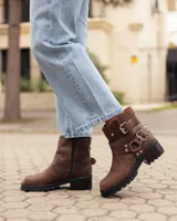 Botas cortas de cuero color caoba, con suela track negra, cierre lateral y correas con hebillas metálicas decorativas.