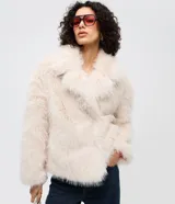 Saco corto de pelo artificial en color beige, con cuello amplio, mangas largas y diseño holgado. Cuenta con forro interior de poliéster.