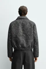 Cazadora de corte relajado confeccionada en tejido jacquard con textura. Presenta cuello solapa, cierre frontal con cremallera, bolsillos de vivo en la cadera y bajo con acabado elástico.