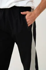 Pantalón negro de corte deportivo con cintura elástica y cordón ajustable. Presenta una franja vertical gris a lo largo de la pierna y puños elásticos.