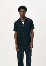 Camisa de manga corta con cuello clásico, cierre frontal de botones y bolsillo en el pecho. Presenta un corte entallado y un acabado de textura sutil.