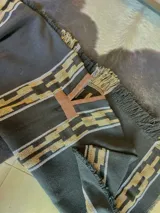 Poncho gris oscuro con diseño geométrico tejido en tonos beige y marrón, escote en V con ribete de cuerina marrón y flecos en los bordes.