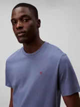 Remera de manga corta color azul, hecha de algodón liso, con cuello redondo y el monograma de Calvin Klein bordado en rojo en el pecho.