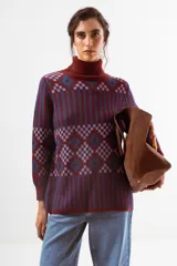 Sweater de punto con cuello alto tipo polera y manga larga. Presenta un diseño geométrico jacquard que combina rayas verticales, cuadros y rombos en tonos bordó y azul.