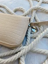 Billetera pequeña de cuero con textura efecto cocodrilo, cierre metálico perimetral y correa de muñeca extraíble. Incluye detalle de moneda metálica decorativa.