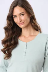 Remera de manga larga en color verde menta, con cuello redondo y cierre frontal parcial de botones a tono. Presenta un diseño con ruedo curvo y un pequeño aplique metálico en la parte inferior.