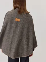 Capa de tejido de punto en color gris melange, con diseño abierto y cierre frontal mediante un botón tipo duffle de madera con detalle en cuero. Presenta bolsillos laterales amplios y bordes con costuras a la vista.