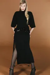 Vestido midi negro de cuello subido y manga corta amplia, con espalda descubierta. Presenta un fajín drapeado con lentejuelas negras a tono en la cadera y abertura lateral en el bajo.