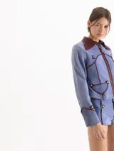Chaqueta de gamuza color celeste con cuello camisero y detalles de ribetes en cuero marrón. Cuenta con cierre frontal y bolsillos aplicados con solapa.