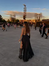 Vestido largo negro con escote profundo halter y diseño de transparencias en el torso. Presenta una falda con tajo lateral pronunciado y detalle de volados en el borde.