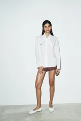 Camisa de popelín de algodón con cuello subido y detalle de aplicación tipo pañuelo anudado al cuello. Presenta manga larga con puños clásicos y cierre frontal mediante botones.