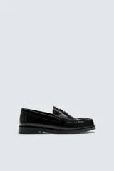 Mocasín de vestir tipo penny loafer, fabricado en piel con acabado brillante, horma redonda y suela con ligero tacón.