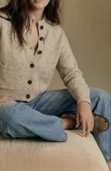 Cardigan de punto en tono beige melange con efecto jaspeado, de corte al cuerpo y manga larga. Presenta cierre frontal con botones oscuros y dos bolsillos delanteros aplicados.