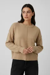 Sweater de lana color beige, de corte holgado y cuello redondo a la base. Presenta costuras verticales decorativas en el frente y puños y ruedo acanalados.