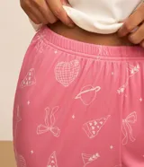 Conjunto de pijama largo de dos piezas, compuesto por una remera de mangas largas con cuello redondo y botones, y un pantalón con cintura elástica y puños ajustados. El pantalón tiene estampado de lazos, bebidas y espejos.