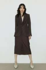 Pollera midi de sastre color marrón oscuro, tiro alto, corte recto con tajo frontal. Presenta cierre y corchete ocultos, y bolsillos al bies.