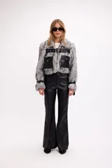 Campera de pelo sintético negro con detalles en cuero sintético, bolsillos frontales con solapa y cinturón ajustable con hebilla metálica.