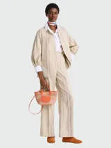 Bolso tipo cesta de tamaño XS, confeccionado en tejido de paja con detalles en cuero color naranja. Cuenta con asas cortas, correa larga ajustable y cierre de botón a presión con solapa de cuero grabada.