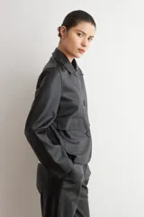 Chaqueta de eco cuero negro con cuello camisero, cierre frontal oculto y mangas largas con puños rectos.