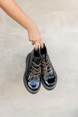 Borcegos de cuero charolado negro con cordones jaspeados en tonos marrones y suela track dentada con costura blanca visible.