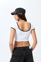 Top corto negro de punto acanalado con escote redondo, mangas cortas y ribetes blancos en cuello y mangas.