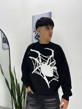 Sweater de tejido de punto color negro con diseño gráfico de una telaraña y una araña en color blanco en la parte frontal. Presenta cuello redondo, mangas largas y puños acanalados.