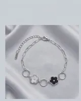 Pulsera de acero con eslabones circulares y dijes en forma de flor esmaltados en blanco y negro.