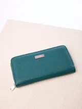 Billetera rectangular de cuero sintético con textura granulada, color bordó. Cuenta con cierre perimetral metálico y placa metálica con el logo de la marca en el frente.