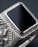 Anillo de acero tipo sello con piedra central rectangular color negro y diseño lateral grabado con motivo de flor de lis.