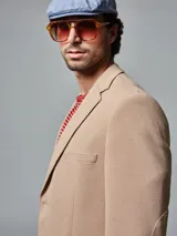 Saco color beige de piqué con cuello con solapas y bolsillos de plastrón. Mangas con coderas y bajo con abertura en espalda.