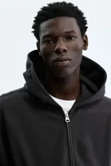 Campera con capucha y cierre de cremallera metálica, corte oversize, hombros caídos y bolsillos delanteros tipo canguro, en tejido negro de algodón.