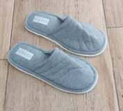 Pantufla de descanso color gris, confeccionada en algodón con diseño acolchado y suela blanca.