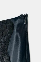 Falda mini de tejido satinado color bordó, con detalle de encaje negro en el frente y bajo asimétrico con abertura.