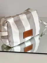 Neceser rectangular de tela a rayas verticales grises y blancas, con parche de cuero marrón con logo de la marca.