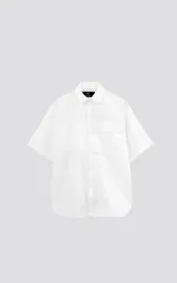 Camisa de manga corta, color blanco, confeccionada en popelín de algodón con silueta oversize. Posee dos bolsillos frontales, uno con solapa y otro con ojal y botón.