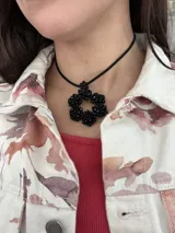Gargantilla negra con dije de flor tramada con cuentas negras y tiento de gamuza.