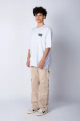 Remera de corte oversize color blanco, con cuello redondo y mangas cortas. Presenta un pequeño logo estampado en el pecho y un diseño gráfico grande en la espalda que incluye la frase 'Good Children' e ilustraciones de un ángel y llamas.