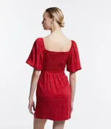 Vestido corto rojo con lunares blancos, escote cuadrado, mangas cortas abullonadas y abertura lateral en la falda.