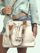 Bolso tipo bucket color crema, confeccionado en cuero texturizado. Tiene doble asa de mano y correa bandolera desmontable con apliques de cuero marrón y beige.