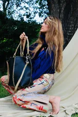 Cartera de cuero negro cosida a mano con costuras visibles decorativas, asas rígidas trenzadas en tonos marrones y correa larga de mano trenzada en color crudo.