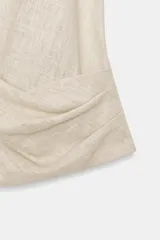 Camisa color crudo confeccionada con lino, de corte holgado, cuello solapa y escote en V. Tiene manga sisa y detalle de pliegue en el delantero. Cierre frontal con botón.